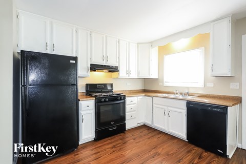 A black fridge stands in a kitchen with white cabinets and wooden floors.