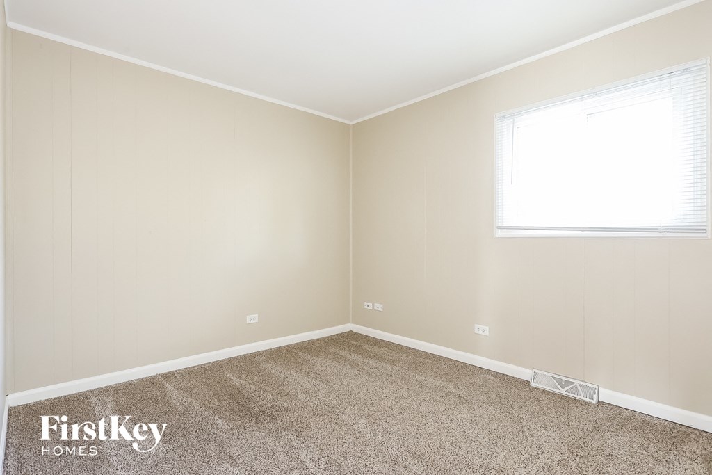 A room with a carpeted floor and a window with blinds.