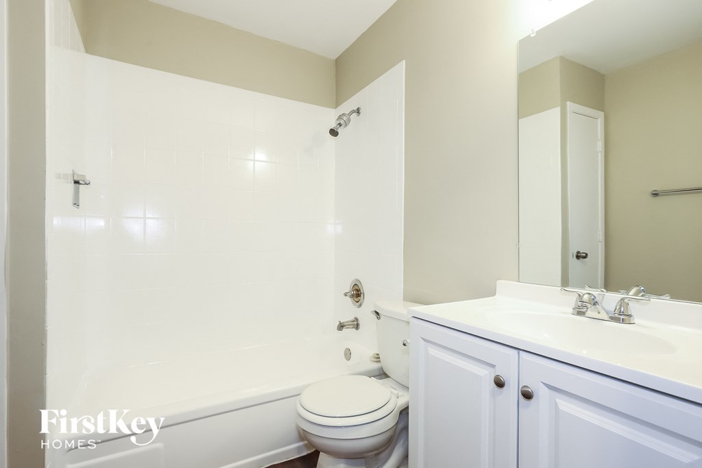 A white toilet sits in a bathroom with a white sink and a white bathtub.