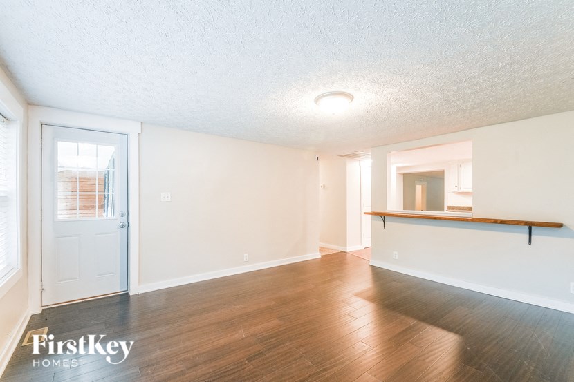 A room with wooden floors and white walls, with a door on the left and a window on the right.