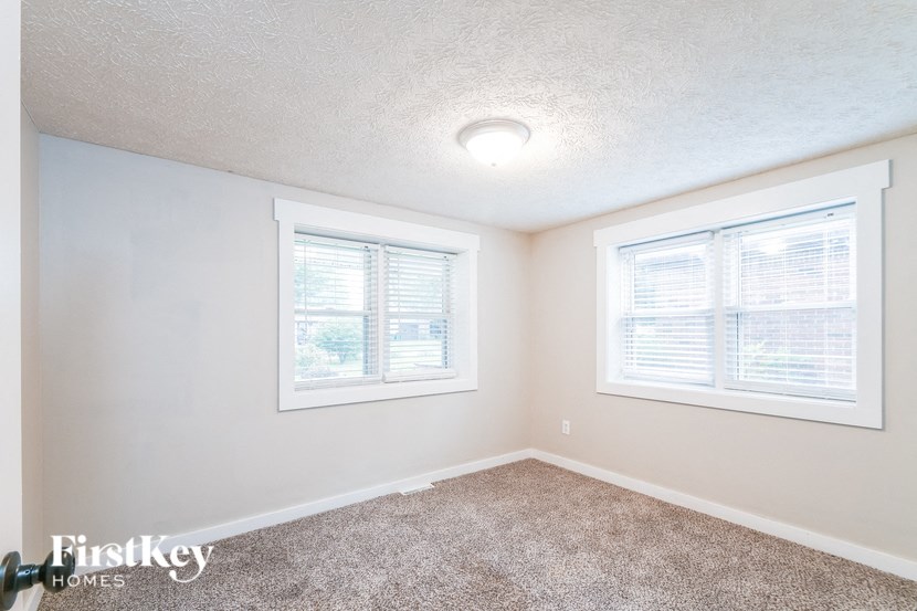 A room with a carpeted floor and two windows.