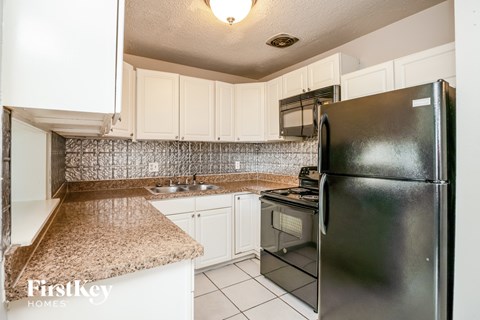 A kitchen with a black fridge and white cabinets.