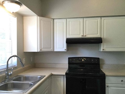A black stove top oven sits under a shelf in a kitchen.