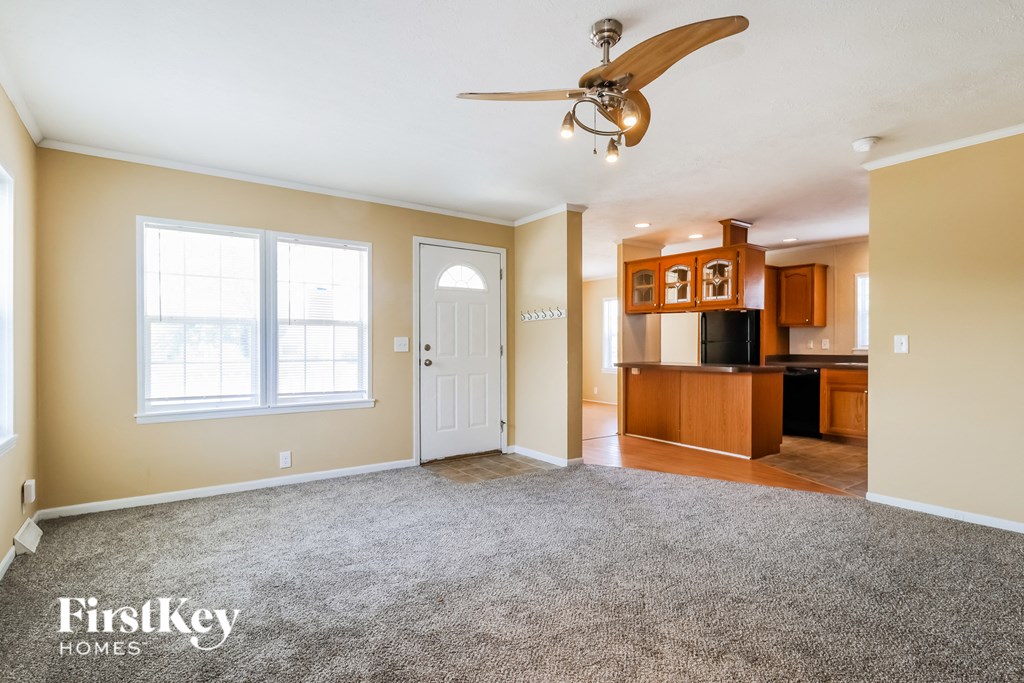 an empty living room with a ceiling fan and a kitchen