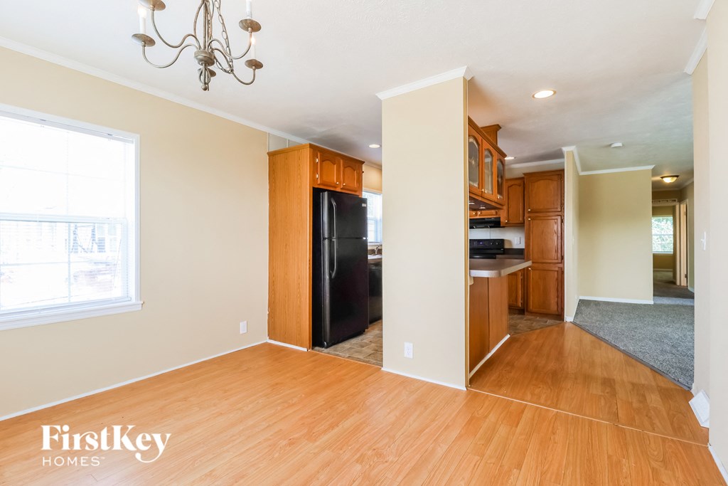 an empty kitchen and living room with wood flooring and a black refrigerator