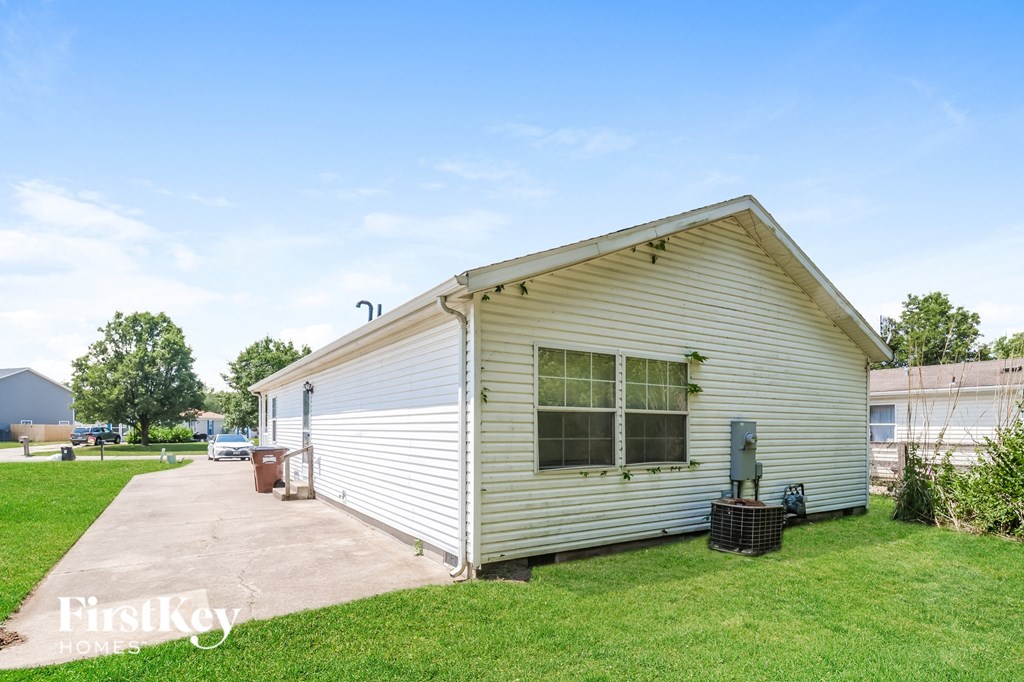 the backyard of a small white house with a driveway and grass