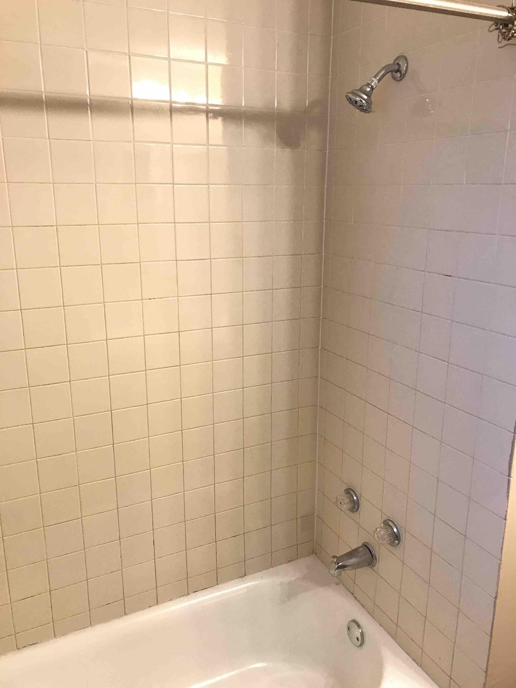 a white tiled bathroom with a tub and a shower