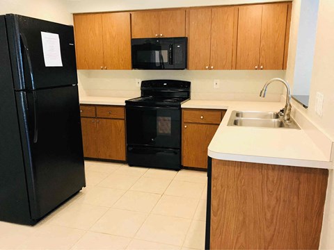 A black refrigerator stands in a kitchen with wooden cabinets and a black oven.
