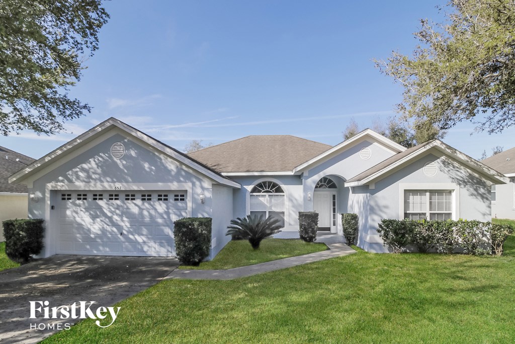 A white house with a garage door and a tree in front of it.