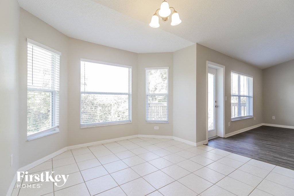A spacious room with a white tile floor and a chandelier hanging from the ceiling.