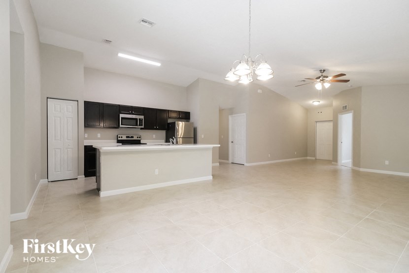 A spacious empty room with a kitchen area in the background.