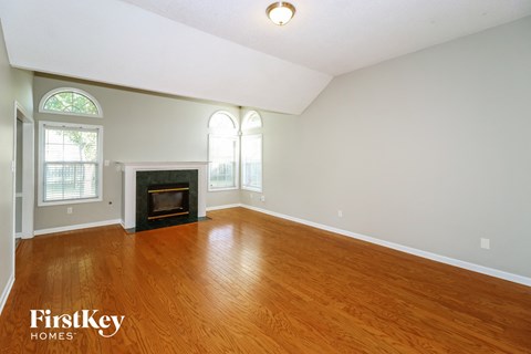 A large empty room with a fireplace and wood flooring.