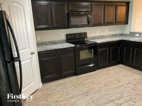 A kitchen with dark wood cabinets and a black refrigerator.