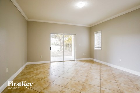 A spacious room with beige tiled flooring and a sliding glass door leading to a backyard.