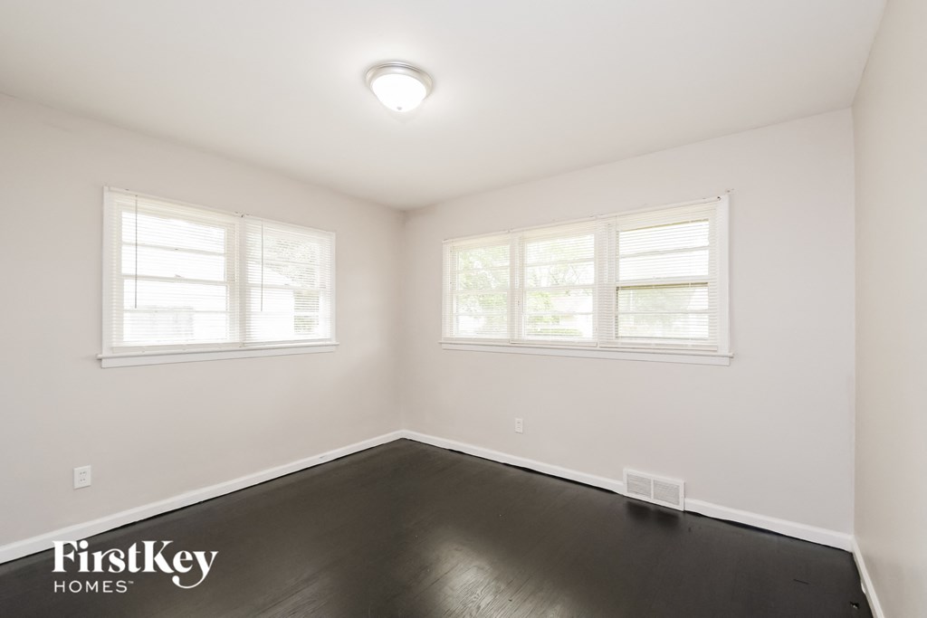 a bedroom with a dark wood floor and two windows