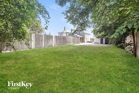 A lush green lawn with a wooden fence and trees in the background.
