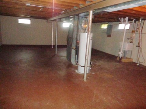 a basement with a dirty floor and a refrigerator