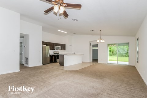 A spacious living room with a ceiling fan and a kitchen in the background.