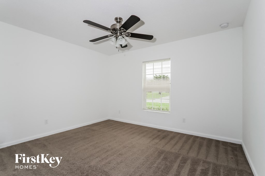 A room with a ceiling fan and a window showing a view of a lawn and trees.