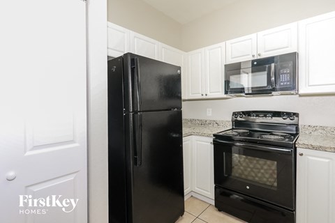 A black fridge and oven in a kitchen with white cabinets.