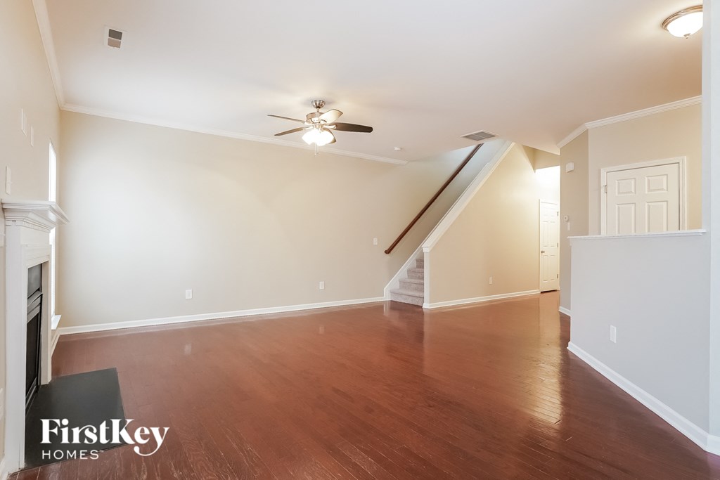 A spacious room with a wood floor and a staircase leading to the second floor.