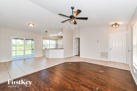 an empty living room with a ceiling fan and a kitchen