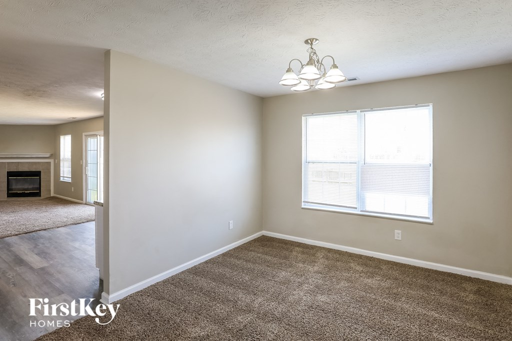 A room with a carpet floor, a chandelier, and a window with blinds.