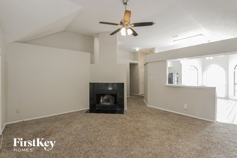 A spacious living room with a fireplace and a ceiling fan.