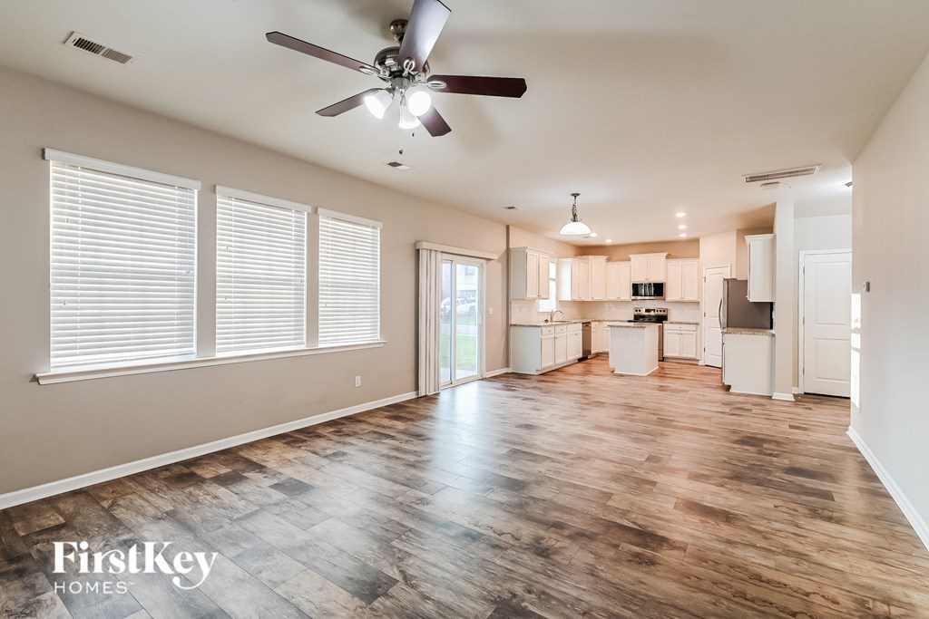 an empty living room with a ceiling fan and a kitchen