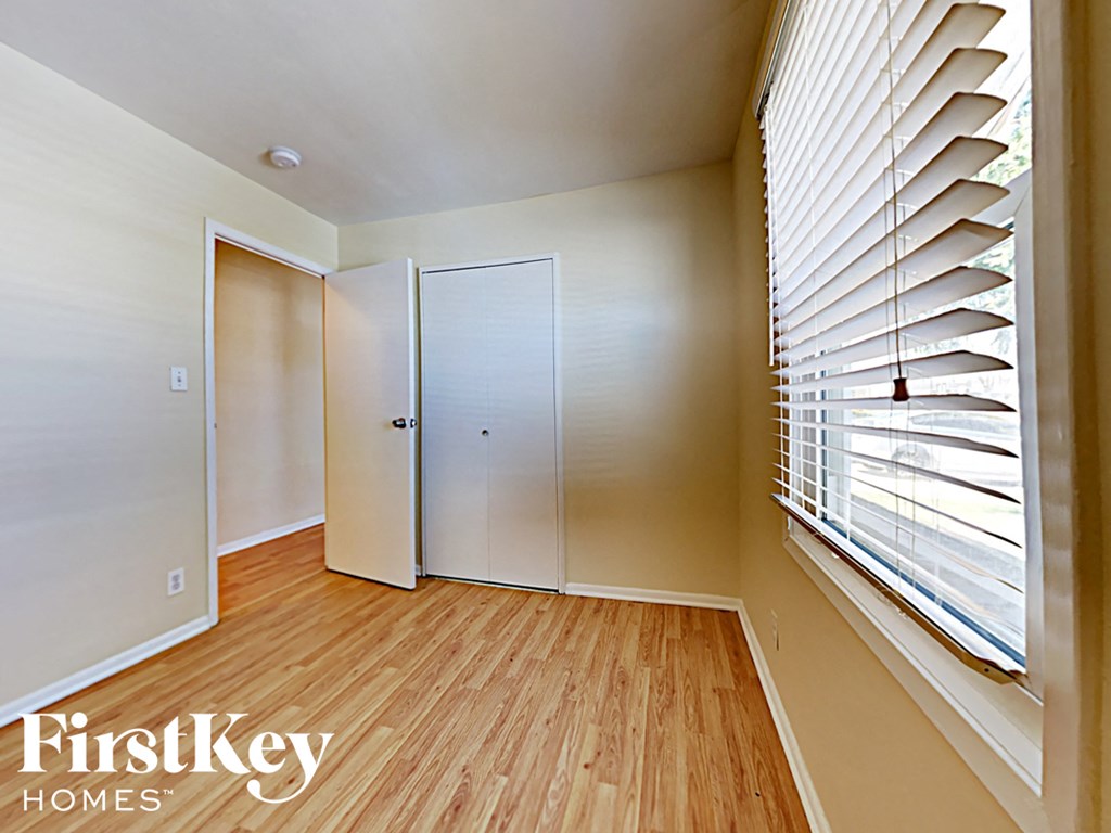 a bedroom with wood flooring and a large window with blinds