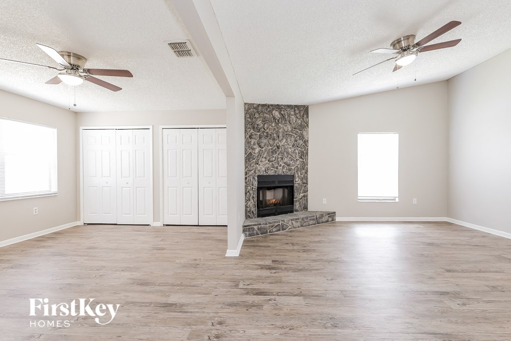 an empty living room with a fireplace and two ceiling fans