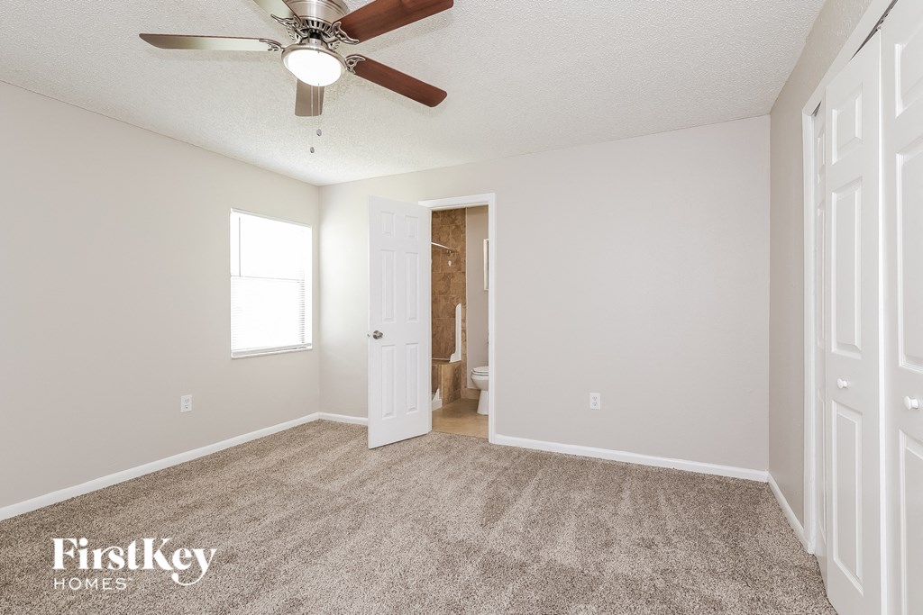 an empty living room with a ceiling fan and a door to a bathroom
