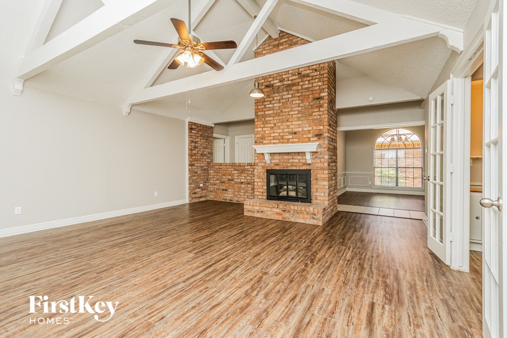 an empty living room with a brick fireplace and a ceiling fan