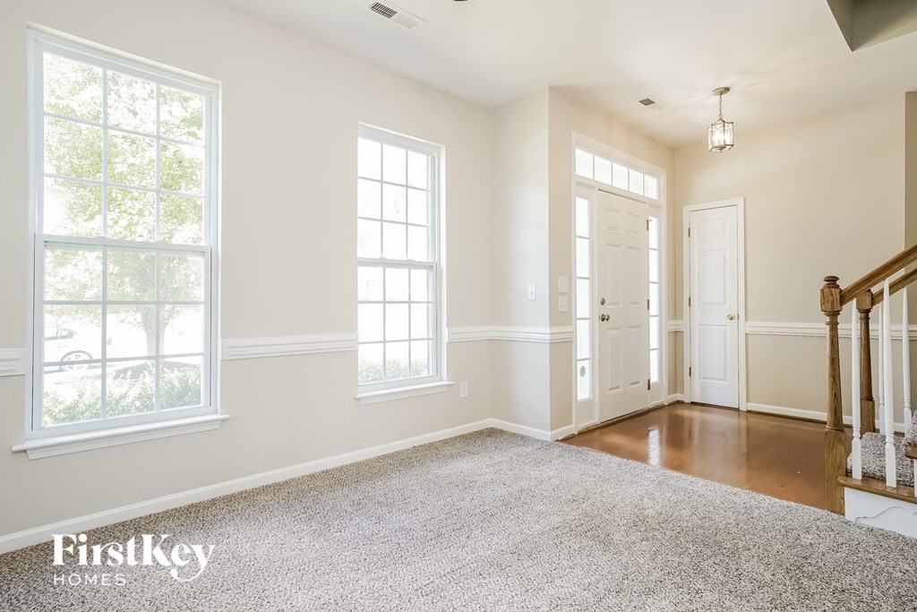 A spacious room with a carpeted floor and a staircase on the right side.