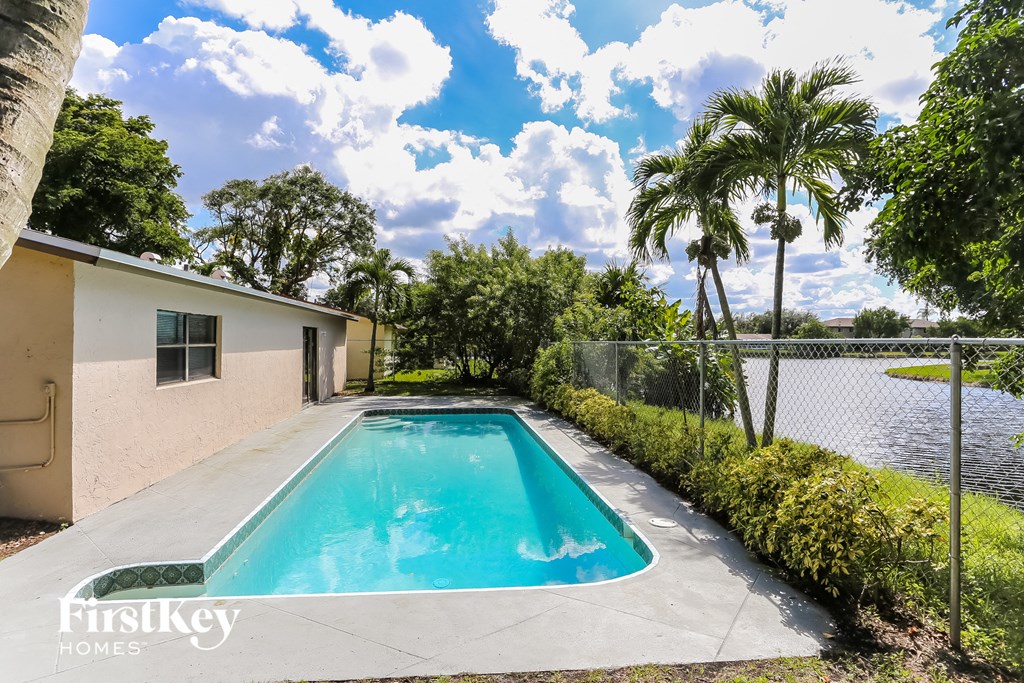 a swimming pool in front of a house with palm trees