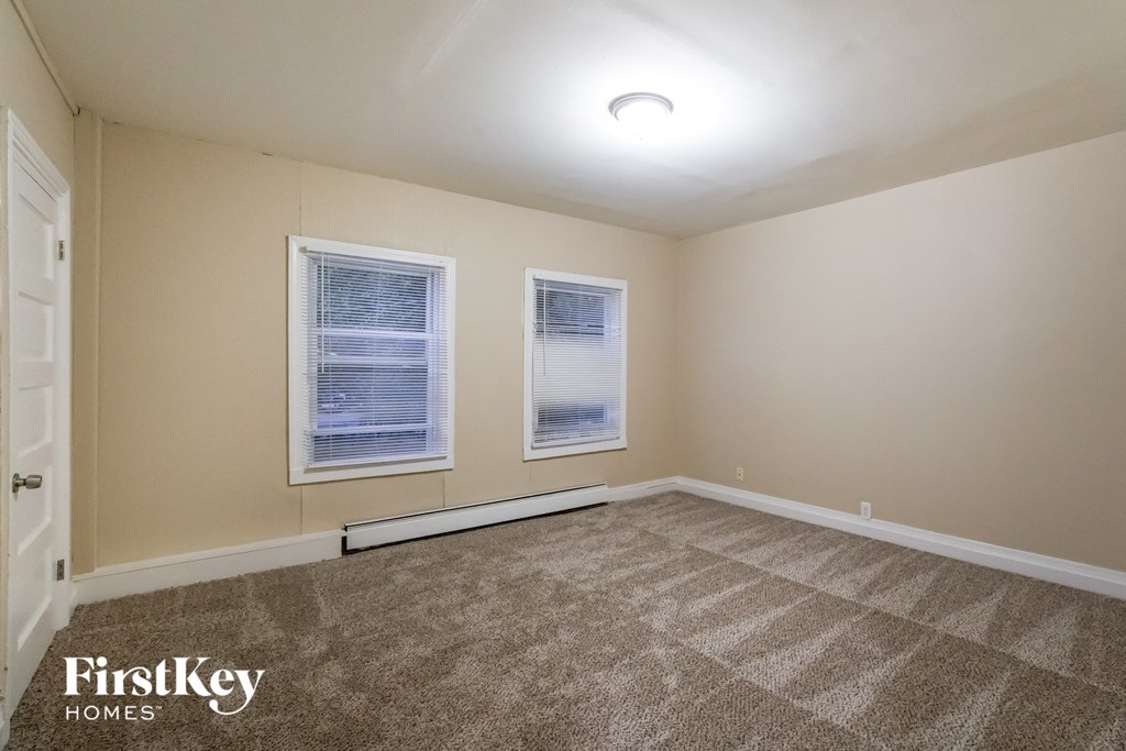 a spacious living room with carpet and two windows