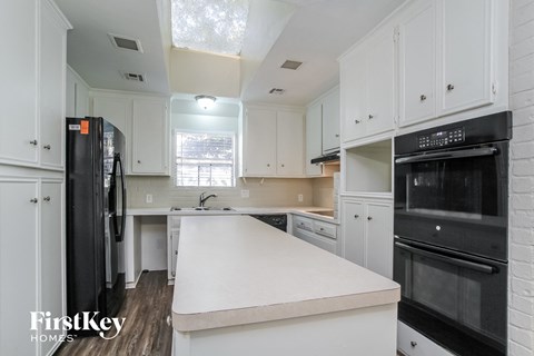 A kitchen with white cabinets and a black fridge.