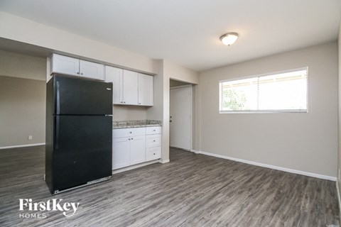 A black fridge sits in a kitchen with wooden floors and white cabinets.