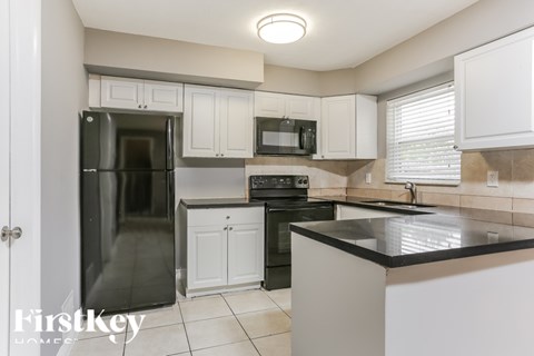 A kitchen with a black refrigerator and white cabinets.