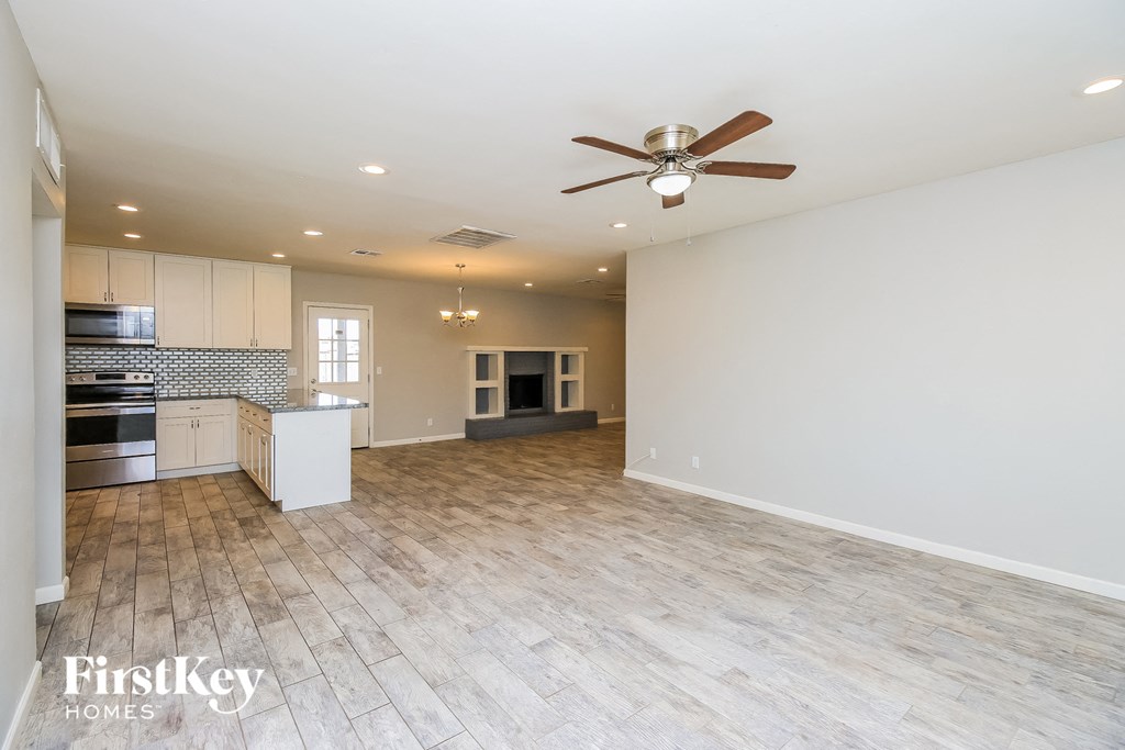an empty living room with a ceiling fan and a kitchen