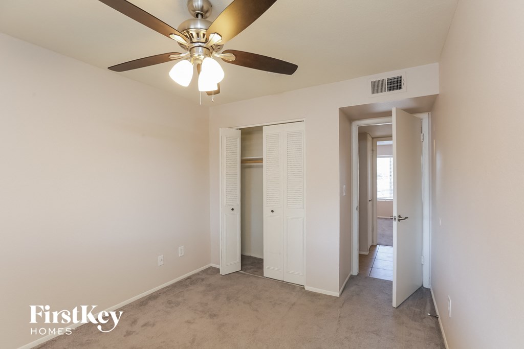 a bedroom with a ceiling fan and a hallway with a closet