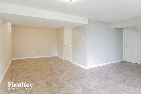 A spacious room with beige walls and tile flooring, with two doors and a ceiling light.