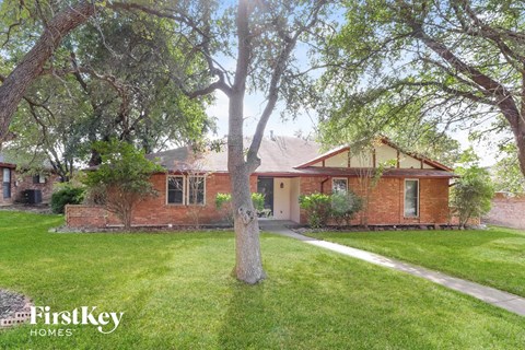 a red brick house with trees and a sidewalk