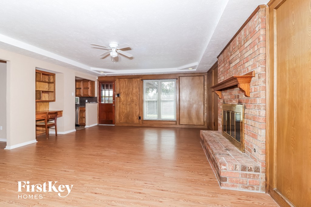 an empty living room with a brick fireplace and wood floors