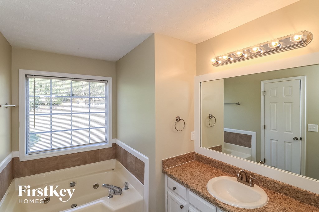the master bathroom has a tub and a sink and a mirror