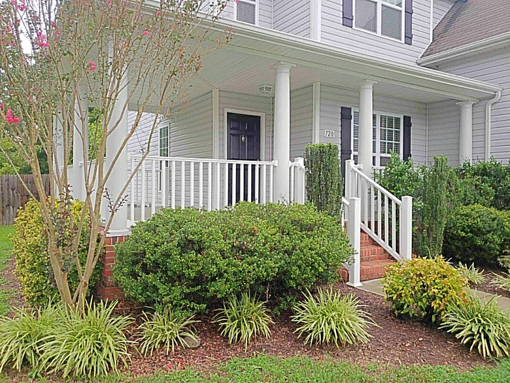A house with a white porch and a tree in front.