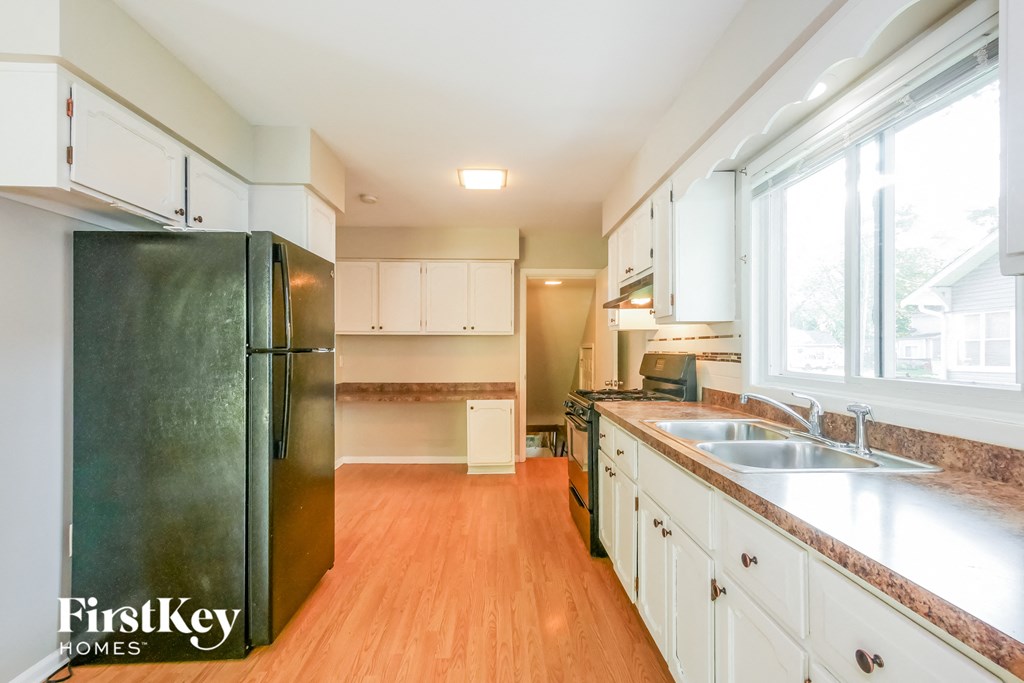 A kitchen with a black fridge and wooden floors.