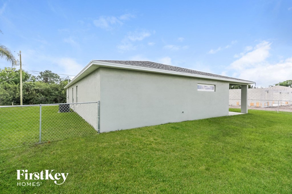 the backyard of a small white house with a chain link fence