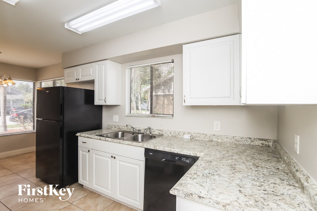 a kitchen with white cabinets and granite counter tops and a black refrigerator