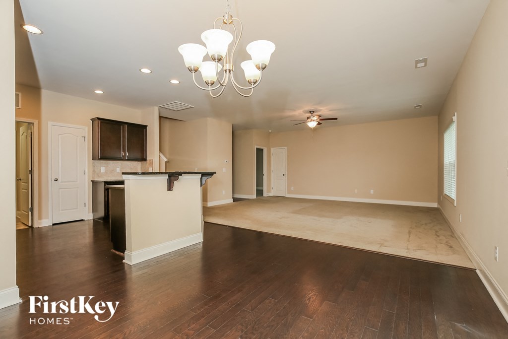 an empty living room with a kitchen and a chandelier